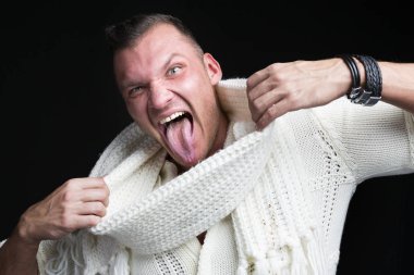 Çok komik bir adam, beyaz kazak ve eşarp, dilini koyu arka plan üzerinde sıkışmış