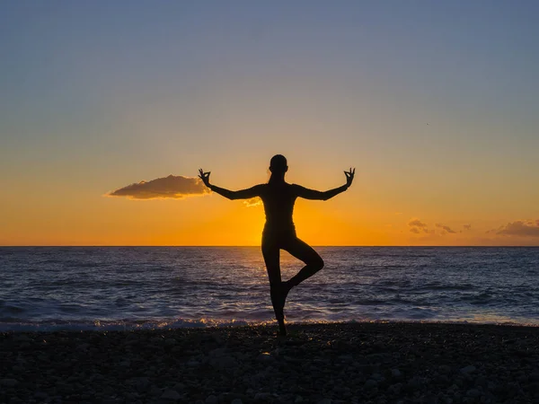 Silhouette de jeune femme faisant des exercices sur la plage de la mer pendant le coucher du soleil. Yoga, fitness et mode de vie sain — Photo