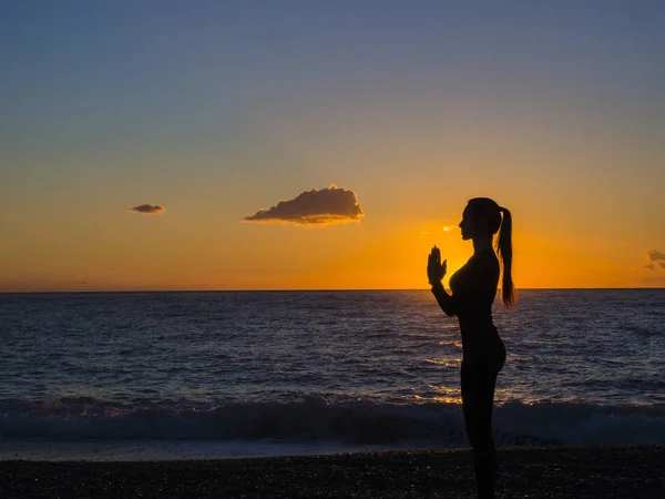 Silhouette woman on the beach at sunset doing yoga asana — Stock Photo, Image