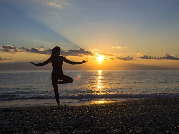 Silhouette de jeune femme faisant des exercices sur la plage de la mer pendant le coucher du soleil. Yoga, fitness et mode de vie sain — Photo