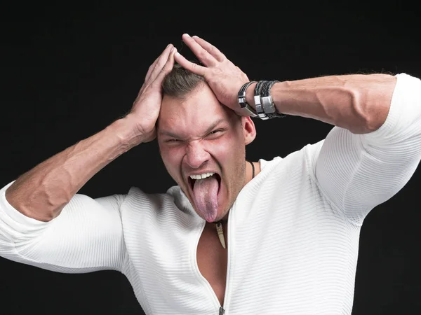 Komik bir adam, beyaz kazak giyen, dilini koyu arka plan üzerinde sıkışmış