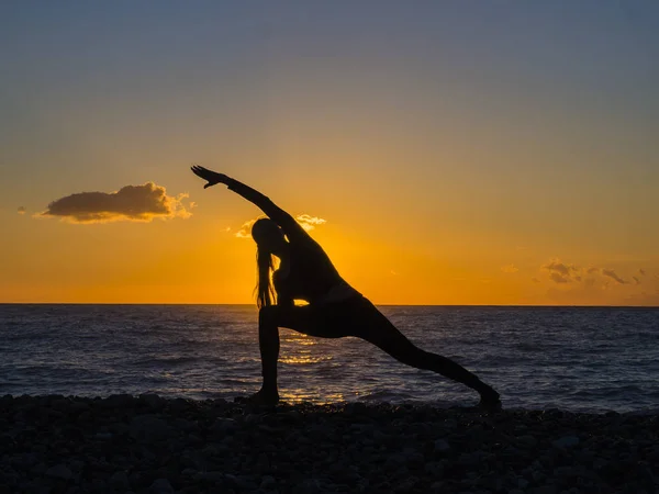 Silhueta de jovem fazendo exercícios na praia do mar durante o pôr do sol. Yoga, fitness e um estilo de vida saudável — Fotografia de Stock