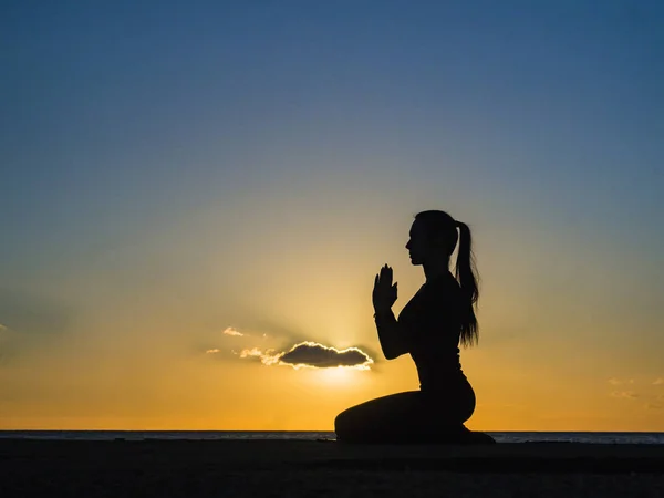 Mulher silhueta na praia ao pôr do sol fazendo ioga asana — Fotografia de Stock