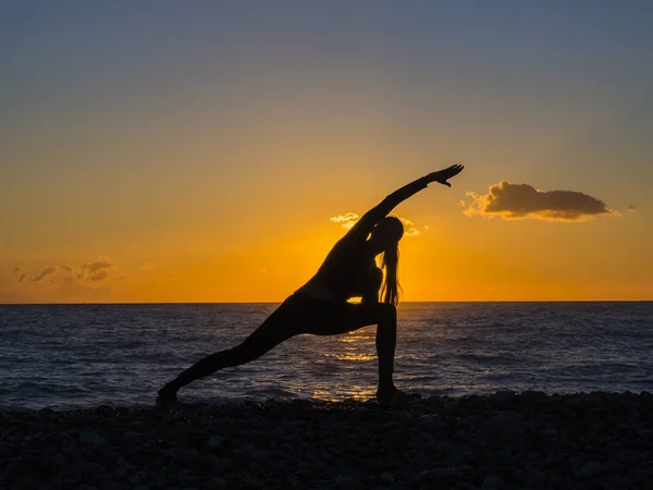 Silhouette d'une jeune femme faisant du yoga sur la plage au coucher du soleil . — Photo