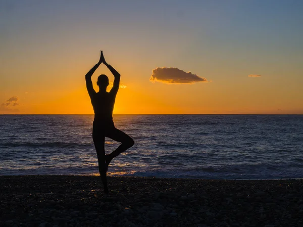 Silhueta de uma jovem mulher fazendo ioga na praia ao pôr do sol . — Fotografia de Stock