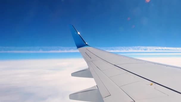 Mirando a través del iluminador del avión volador al atardecer. Vista al ala, cielo y nubes blancas debajo — Vídeo de stock