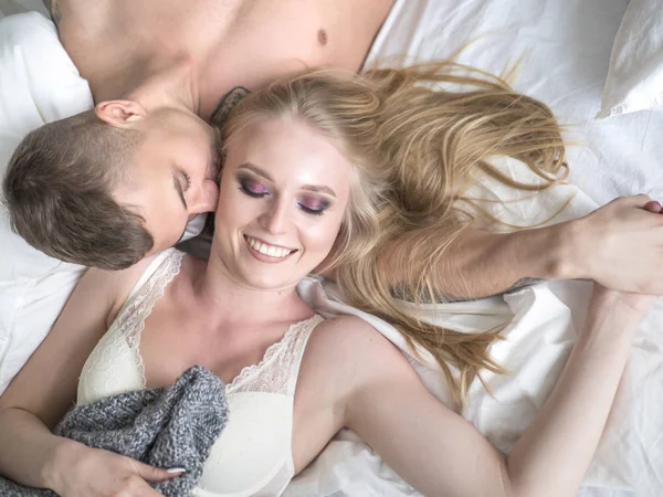 Pareja joven acostada en la cama hombre besando mujer sonriente. Amor y concepto de relaciones — Foto de Stock