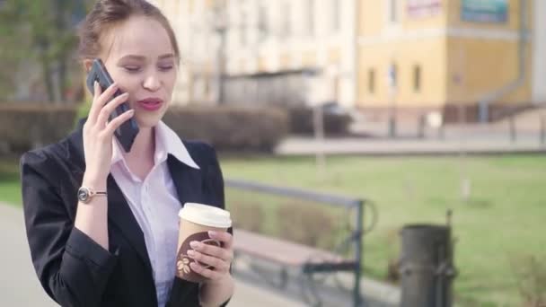Молода успішна бізнес-леді, використовуючи смартфон у центрі міста, професійний роботодавець розмовляє з діловим партнером, який п'є каву. Бізнес-район хмарочоси на задньому плані — стокове відео