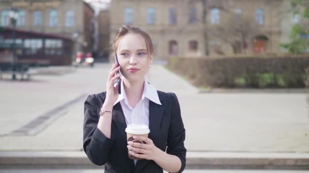 Şehirde yürüyüş, kahve içme, telefonda konuşurken bir genç güzel iş kadın öğrenci kıyafetli, portresini. Konsept: yeni iş, iletişim, bankacı, Yöneticisi. — Stok video