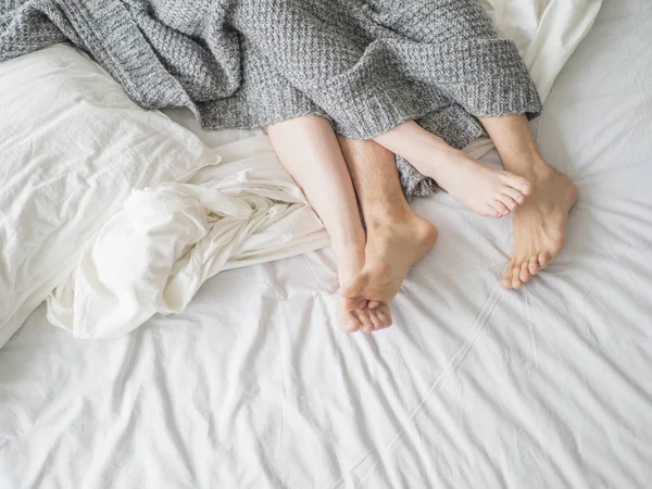 ベッド寝室 - 愛好家の官能的で親密な瞬間の概念で灰色の毛布の下の愛するカップルの男性と女性の足のクローズ アップ. — ストック写真