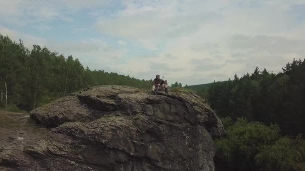 Drone weergave. Sniper vrouw met een sniper rifle zit op de rotsen op de rivier. Cameta verplaatsen van object - sniper vrouw. — Stockvideo