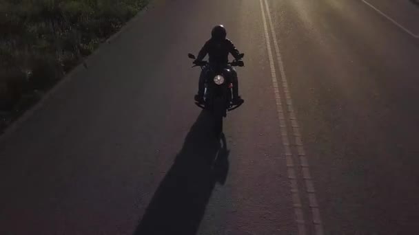 Человек на мотоцикле едет по дороге. Камера возвращается, чтобы сопровождать гонщика. Видео с беспилотника — стоковое видео