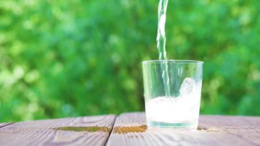 Gazlı mineral su bulanık cam ağaç yaprakları arka planda, sağlıklı yaşam kavramı içine dökülen