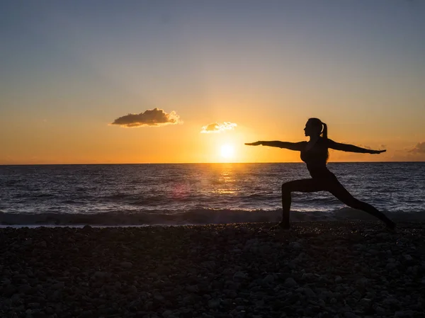 Mulher silhueta praticando ioga ou alongamento no cais da praia ao pôr do sol ou ao nascer do sol. Prática de ioga, meditação e conceito healt — Fotografia de Stock