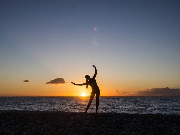 Женщина-силуэт практикует йогу или растягивается на пляжном пирсе на закате или восходе солнца. Практика йоги, посредничество и концепция здоровья — стоковое фото
