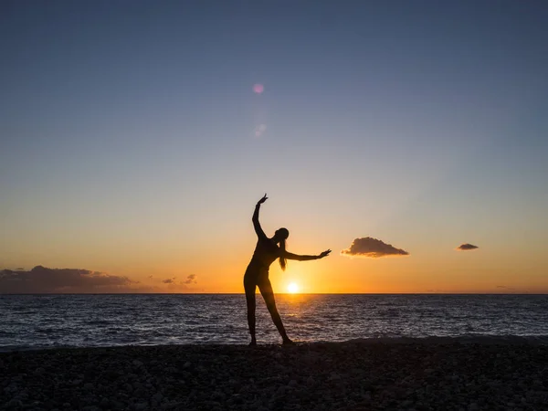 Silhouette de jeune femme faisant des exercices de yoga sur la plage au coucher du soleil. Concept de méditation et yoga — Photo