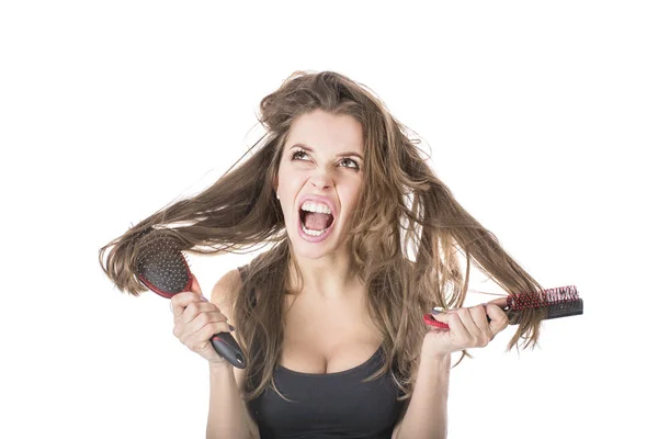 Junge Frau schreit, während sie zerzauste braune Haare mit der Bürste auskämmt. isoliert auf weißem Hintergrund — Stockfoto