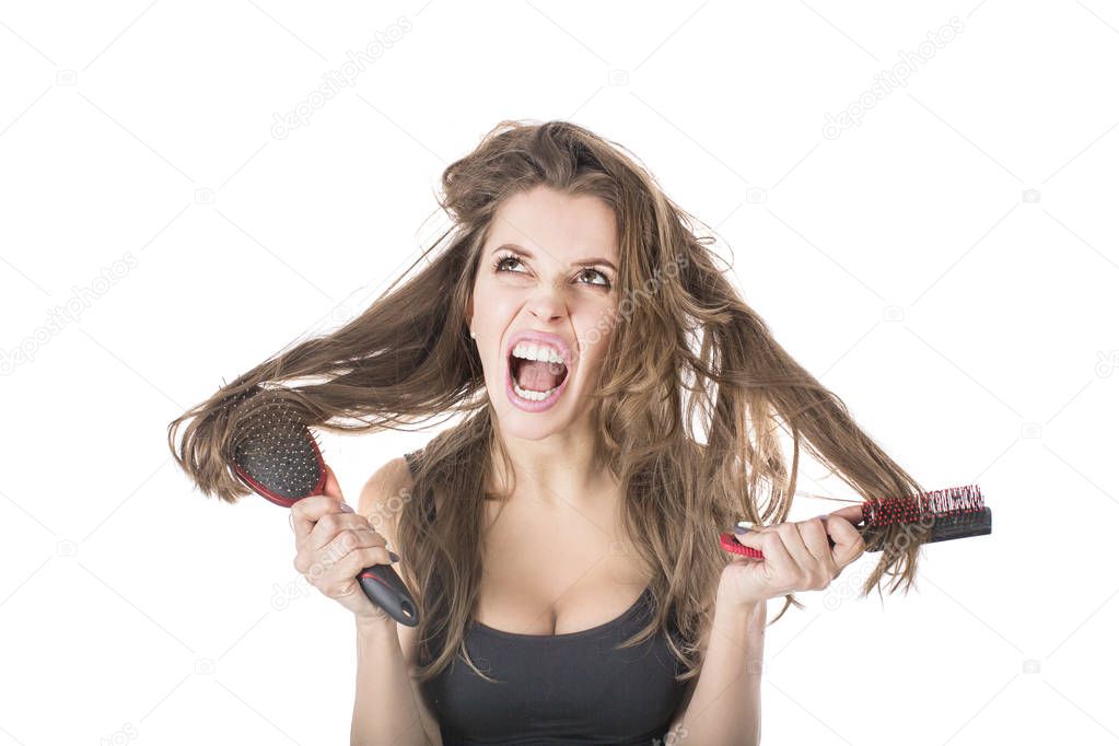 Young woman screaming while comb out tousled brown hair by brush. Isolated on white background