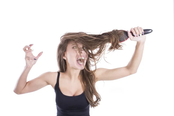 Gritando mujer enojada con un peine en el pelo enredado sobre un fondo blanco. Concepto de cuidado del cabello — Foto de Stock