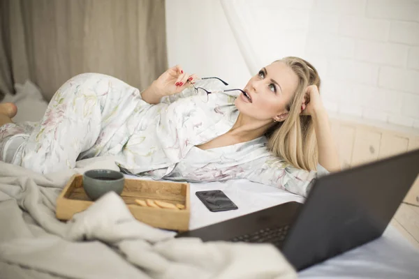 Freelancer woman works at home in bed.