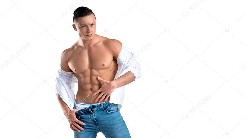 Man in blue jeans and white shirt touching his perfect abs isolated on white.