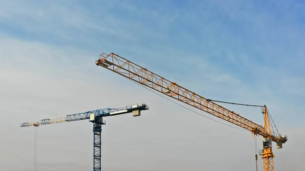 Grote bouwplaats met meerdere kranen die aan een gebouwencomplex werken, met heldere blauwe lucht en de zon — Stockfoto