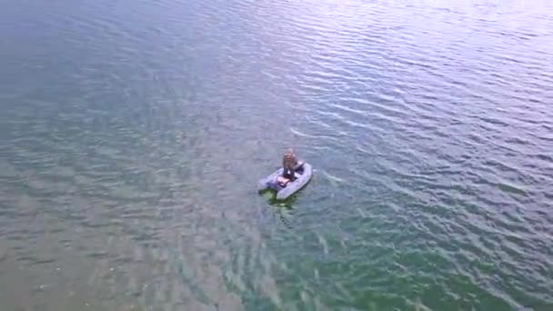 Visser blijven in een rubberboot op het meer bij dageraad in de zomer. Ochtend mist kruipt over het water. Schieten met quadrocopter vliegt laag over het water. — Stockvideo