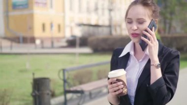 Şehir merkezinde, kahve içme iş ortağı ile konuşurken profesyonel kadın işveren akıllı telefon kullanan genç başarılı işkadını. İş bölgesi gökdelenler arka planda