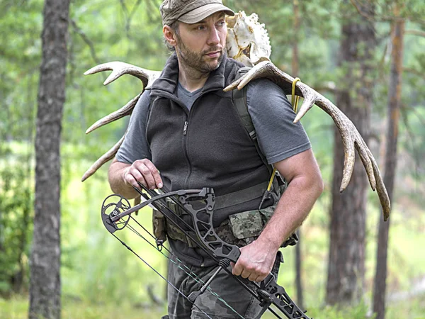Охотник с луком в лесу несет рога лося на спине и смотрит рядом — стоковое фото