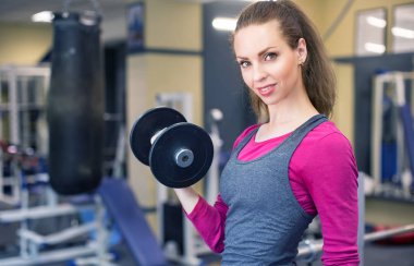 Bir atlet gülümseyen kadın spor salonunda bir dambıl çeker.