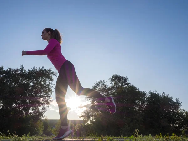 Vista lateral de una mujer corriendo en el área del parque de la ciudad durante el atardecer . — Foto de Stock