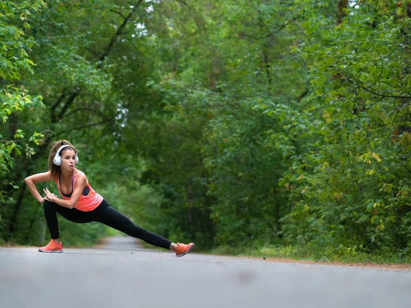 Hermosa joven mujer calienta los músculos antes de trotar en el bosque . — Foto de Stock