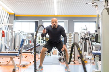 Acımasız orta yaşlı adam spor salonunda çalışırken savaş ipi egzersiz yapıyor.
