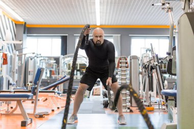 Acımasız orta yaşlı adam spor salonunda çalışırken savaş ipi egzersiz yapıyor. Ön görünüm