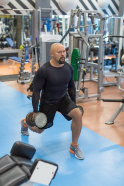 Orta yaşlı adam bacaklar için egzersiz yapıyor. Dambıllarla bacak lar üzerinde çalışan adam.