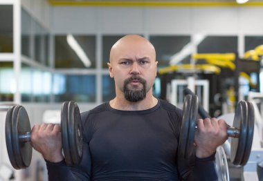 Orta yaşlı adam spor salonunda dumbbells ile pazı için egzersiz yapıyor.