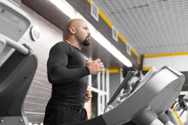 Spor salonunda koşu bandıüzerinde çalışan acımasız bir orta yaşlı adamın fotoğrafı.