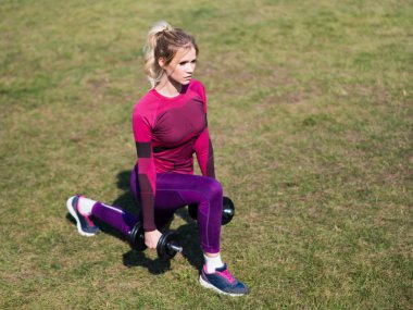 Genç kadın dambıllı bacaklar için execises yapıyor.