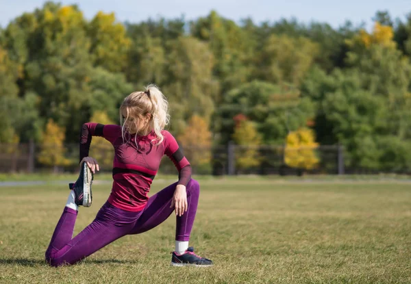 Mujer de fitness de 20 años estirando las piernas en un césped en el parque . — Foto de Stock