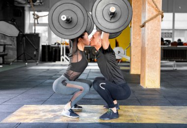 Fitness çifti bir halter sallıyor ve öpüşüyorlar. Sportif aile spor salonunda..