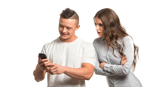 Retrato de pareja. Mujer molesta enojada sosteniendo los brazos cruzados y mira sobre el hombro de los maridos en su teléfono. Hombre mirando a su teléfono . — Foto de Stock