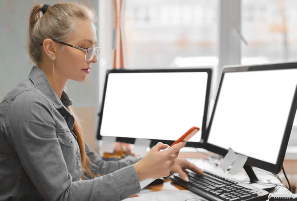 Woman holding smartphone and using computer in office room, for graphics display montage — ストック写真