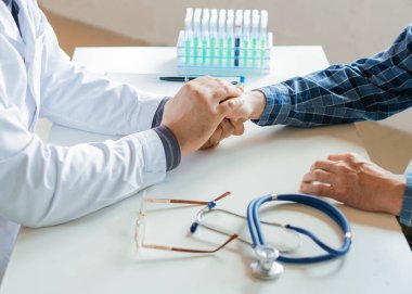 Doktor yaşlı hastayı ellerini tutarak cesaretlendiriyor.
