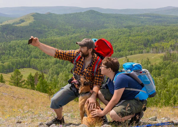 Vader met zoon en hun hond nemen een selfie bovenop de berg. — Stockfoto