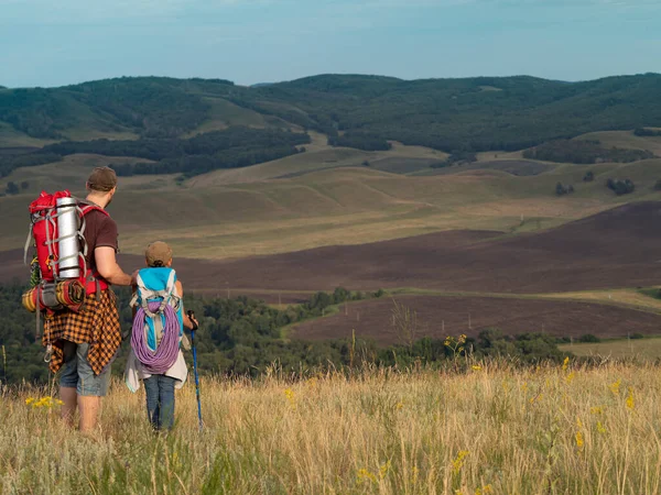 Vader en dochter wandelen door de top van de heuvel met rugzakken, reizen in de natuur. — Stockfoto