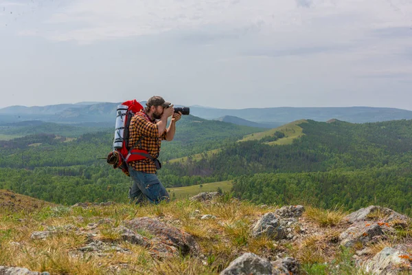 Ένας φωτογράφος με ένα μεγάλο σακίδιο βγάζει μια φωτογραφία στα βουνά. — Φωτογραφία Αρχείου