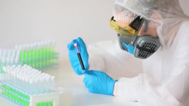 Beyaz tulumlu bir araştırmacının test tüpündeki hastalıklı kan örneğine baktığı yakın plan görüntüsü..