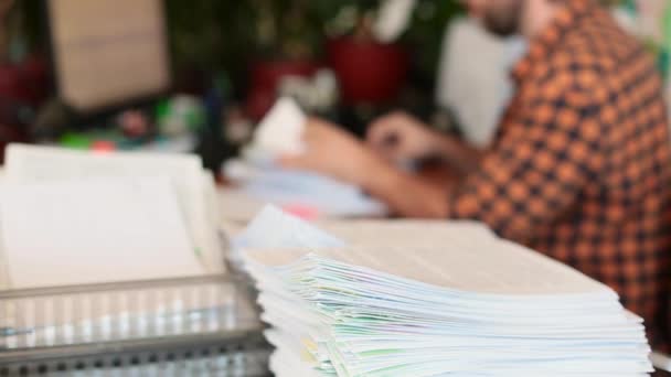 Un homme analyse les papiers dans le bureau et les empile dans une pile. Focus sur une pile de papiers. — Video