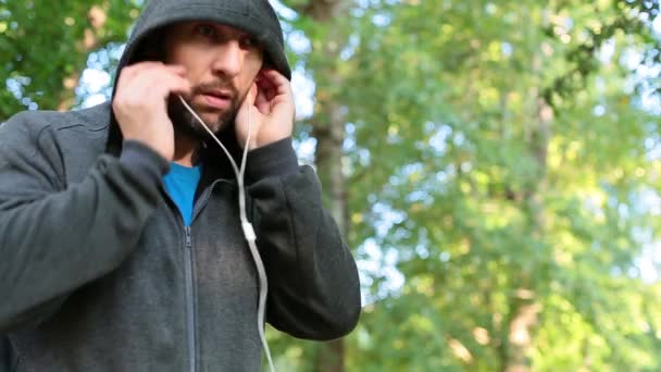 El hombre inserta auriculares en los oídos antes de correr el entrenamiento — Vídeo de stock