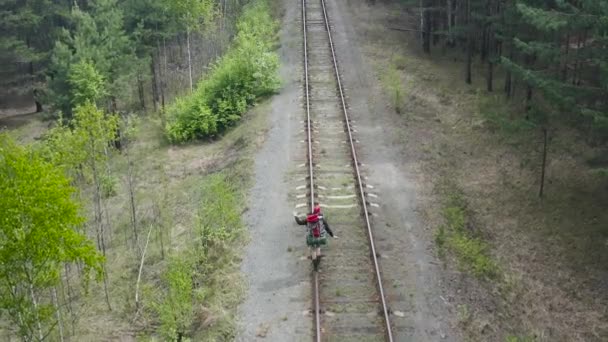 Toerist met een rugzak gaat op de rail van de spoorweg. Balansen en probeert niet te vallen. Luchtzicht. — Stockvideo